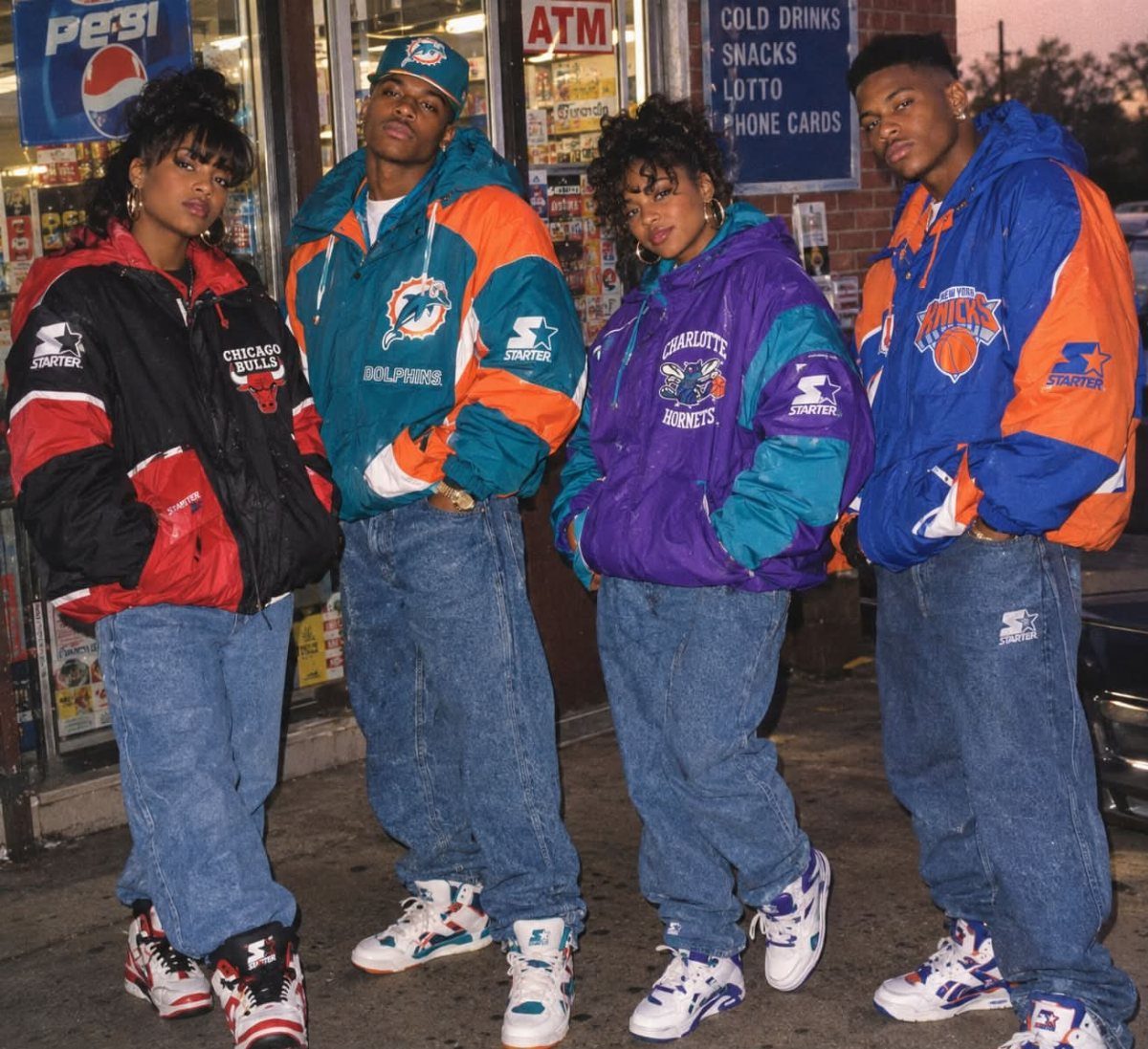 Four people posing in colorful oversized windbreakers, baggy jeans, and chunky sneakers outside a store.