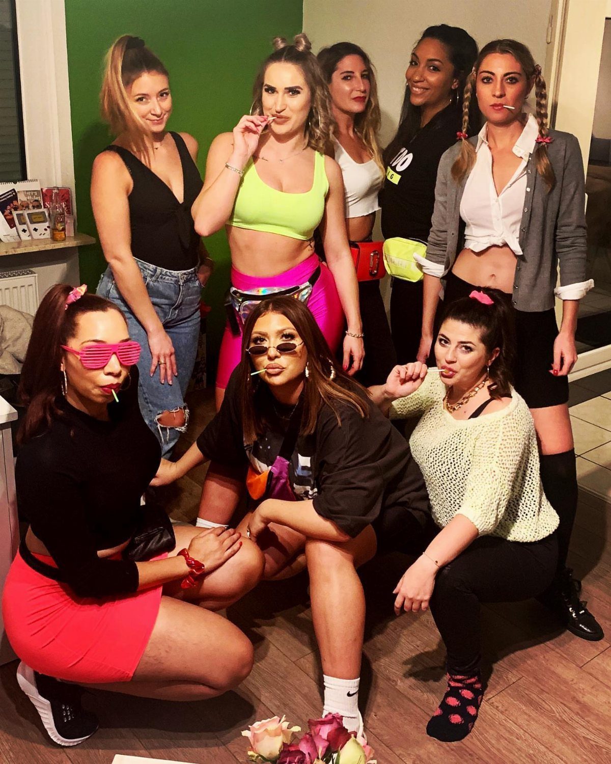 Group of young women posing in colorful outfits against a green wall.