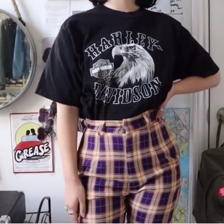 A person wearing a black graphic t-shirt and high-waisted purple plaid trousers.