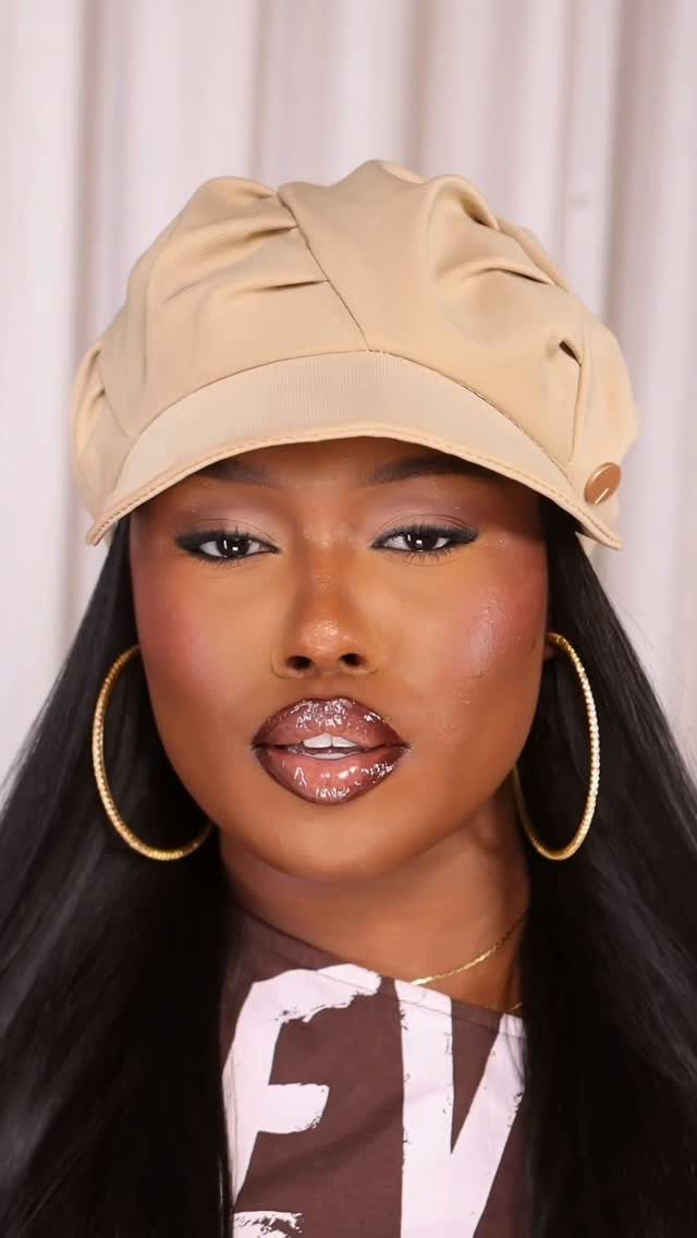 Woman wearing a tan newsboy cap, large gold hoop earrings, and a brown graphic t-shirt.