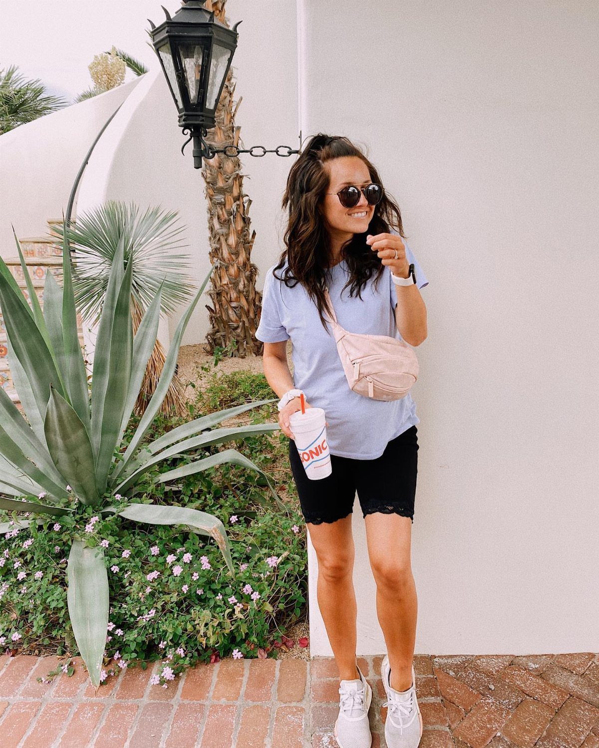 A woman wearing a light blue t-shirt and black biker shorts standing outdoors.