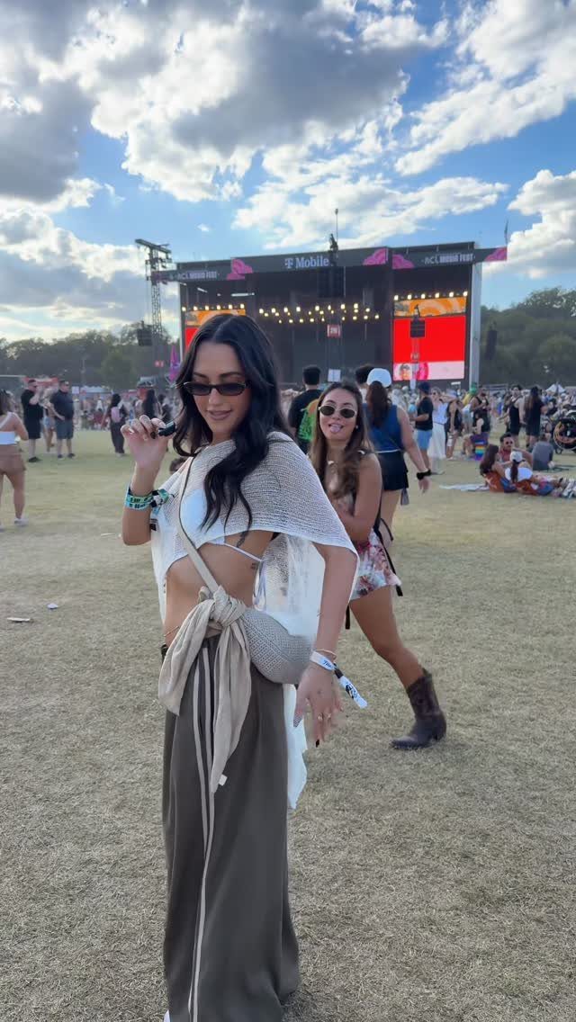 A woman posing in a crochet top and wide-leg trousers at an outdoor music festival.