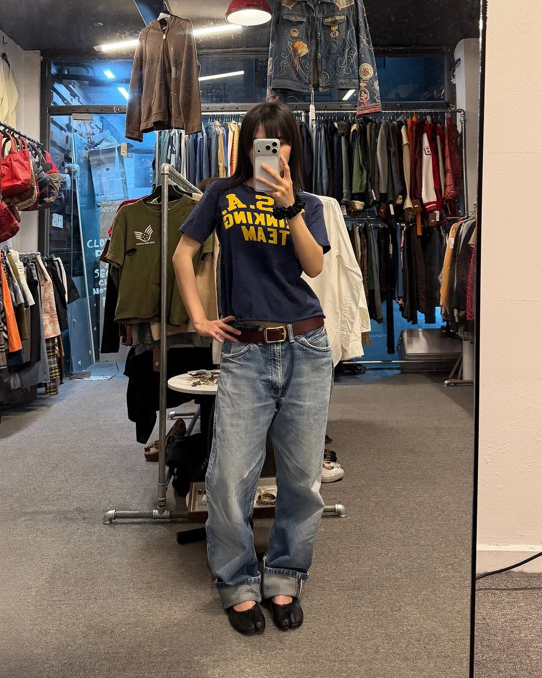 A person posing in a navy graphic t-shirt and light blue denim jeans.