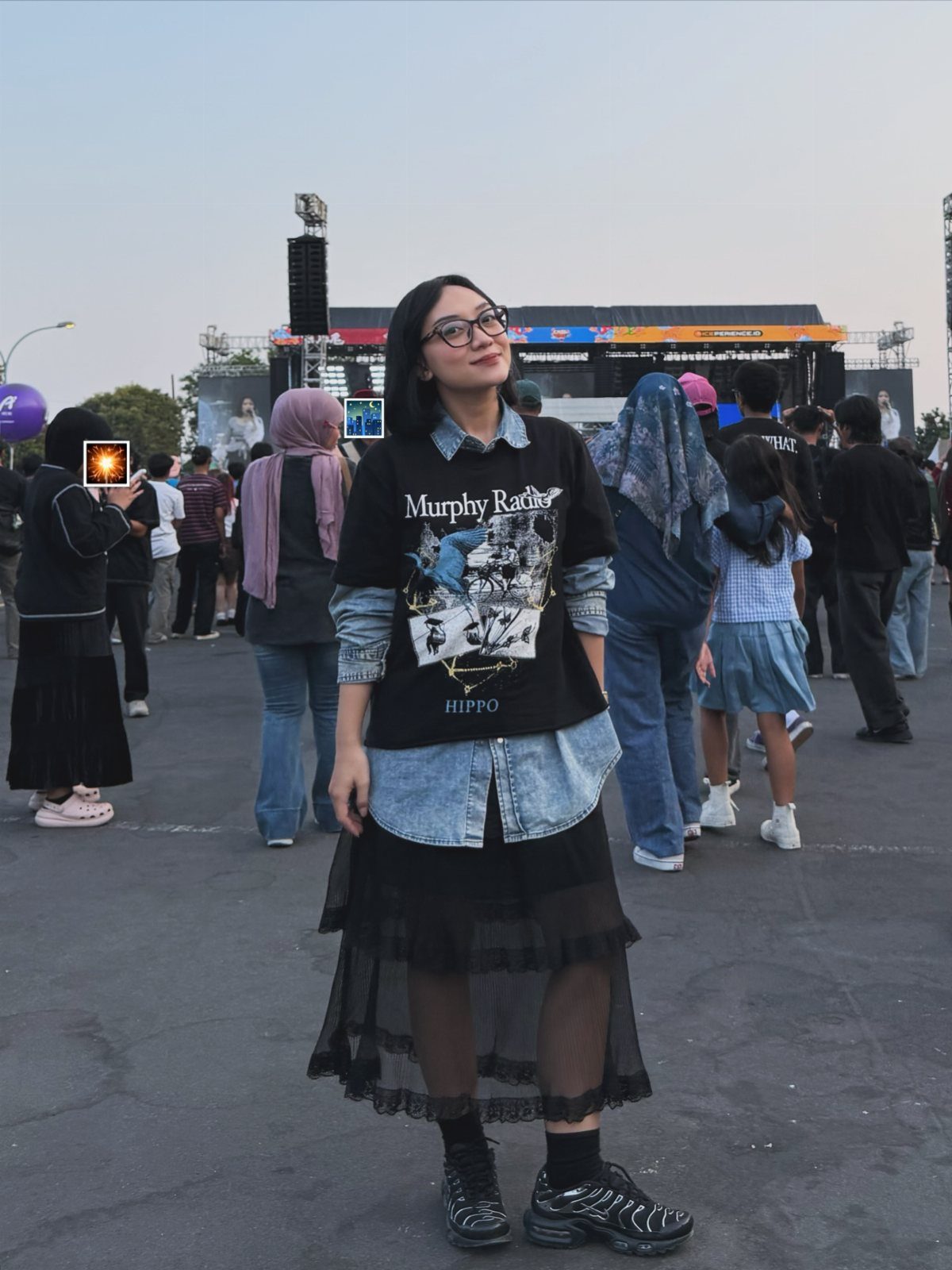 Woman wearing a black graphic tee layered over a denim shirt and a black sheer skirt.