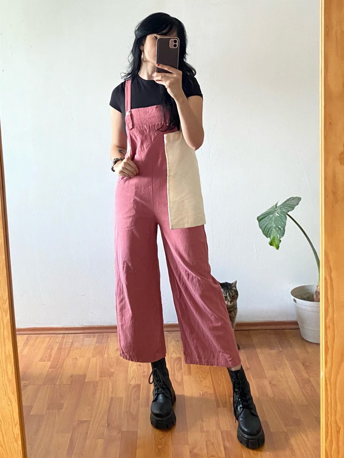 A person wearing pink wide-leg overalls and black platform boots standing in a room.