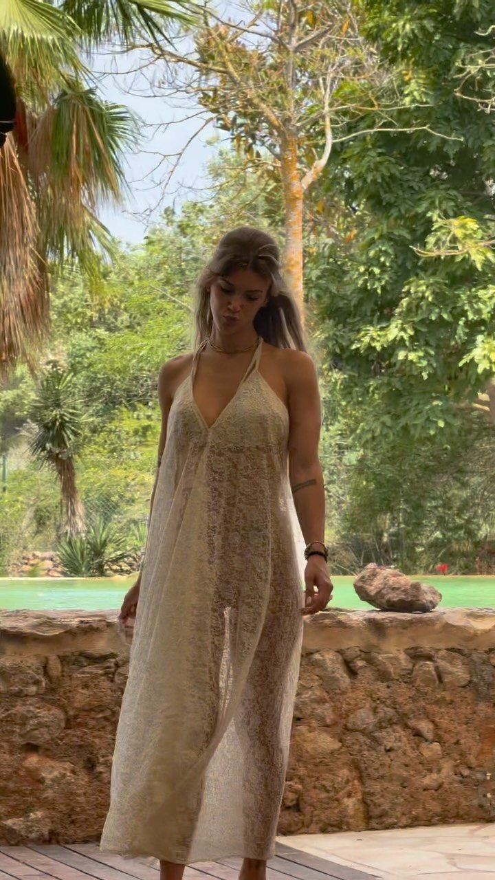 A woman wearing a long white lace maxi dress standing in a tropical outdoor setting.