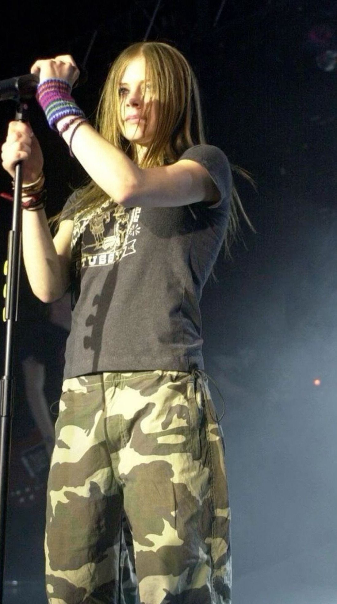 Young woman with long blonde hair performing on stage wearing a graphic t-shirt and camouflage pants.