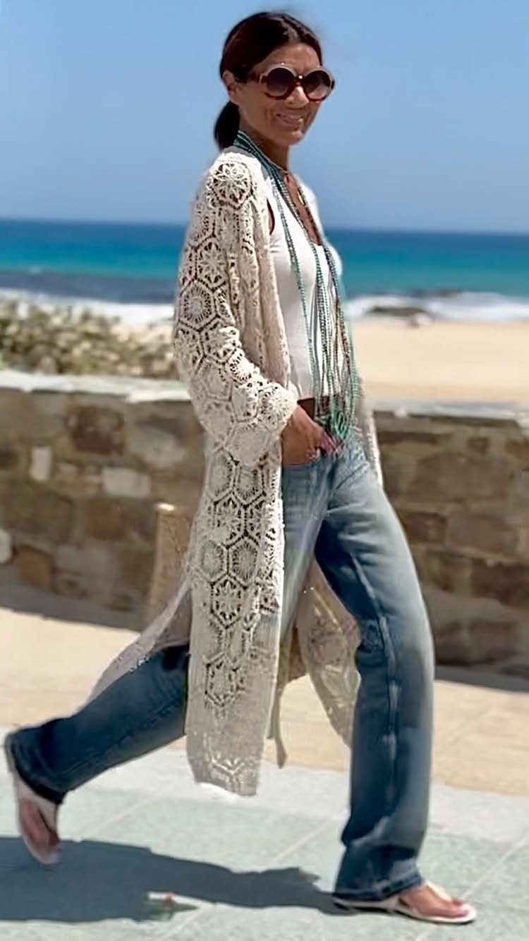 Woman wearing a long cream crochet lace kimono over jeans and a white top at the beach.