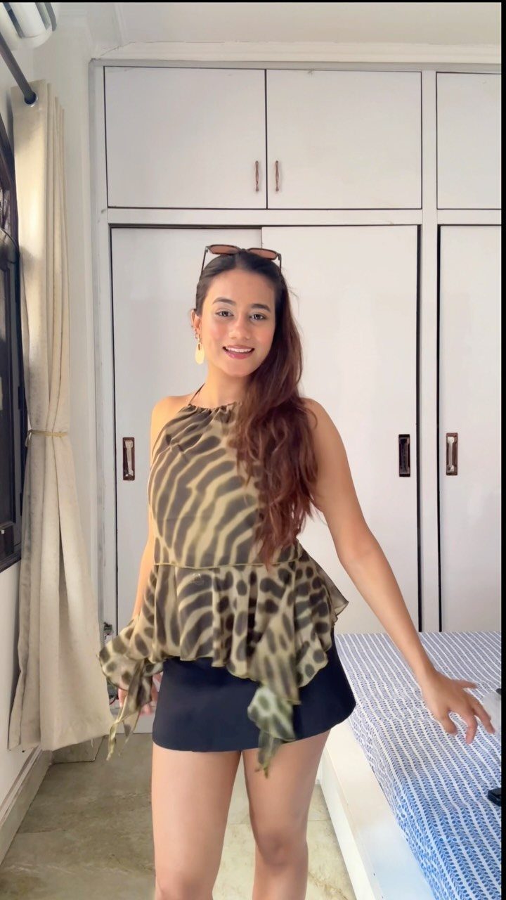 A woman wearing an animal print halter top and black shorts posing indoors.