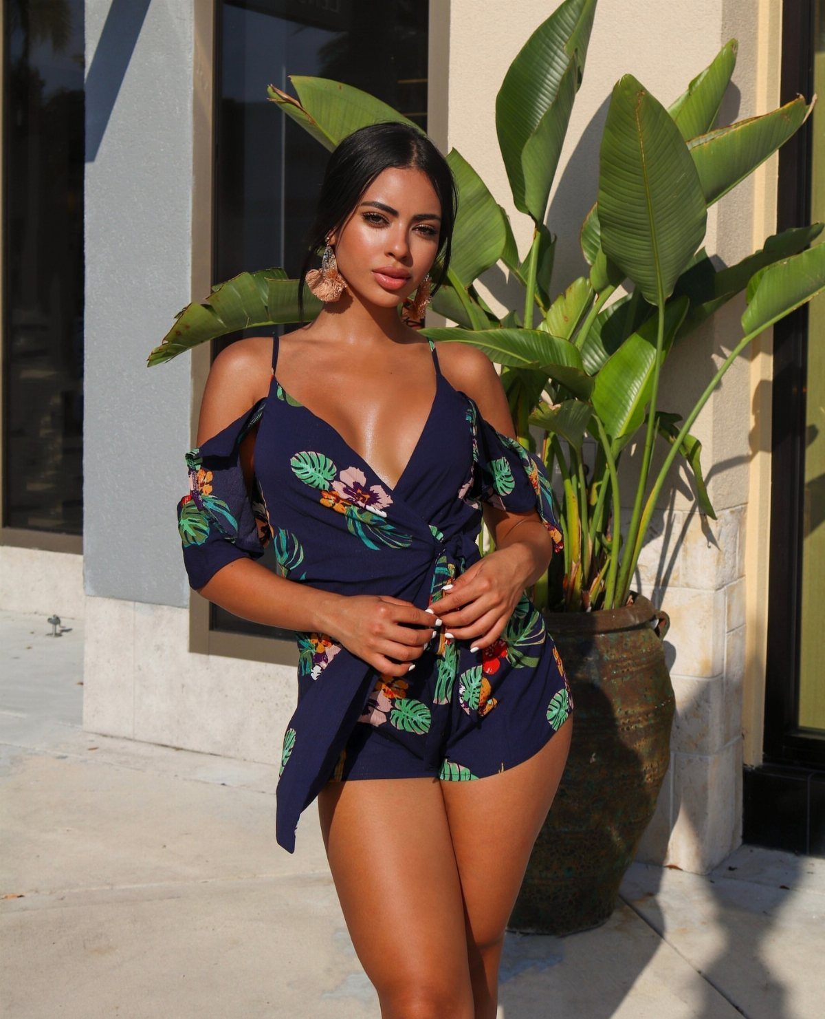 Woman wearing a navy blue floral print romper standing next to a large green plant.