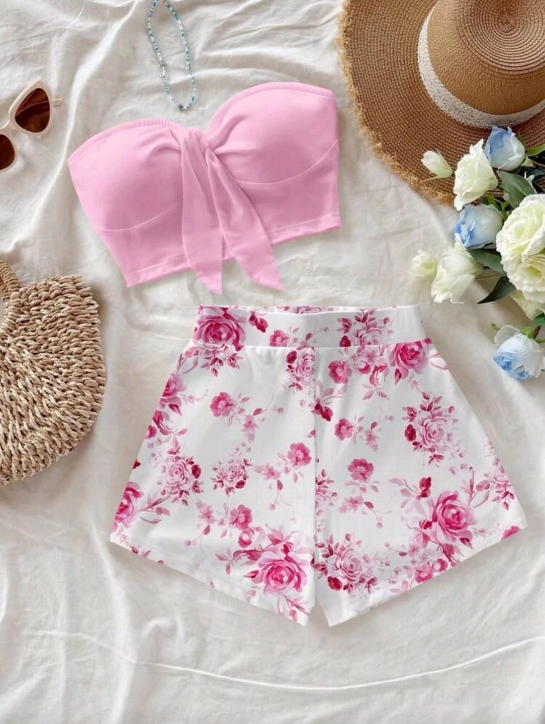 Pink tie-front crop top and white floral shorts arranged on a white cloth with summer accessories.