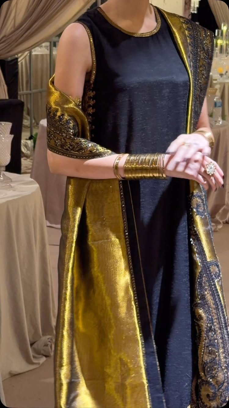 Person wearing a black satin tunic with a decorative gold embroidered shawl and gold bangles.