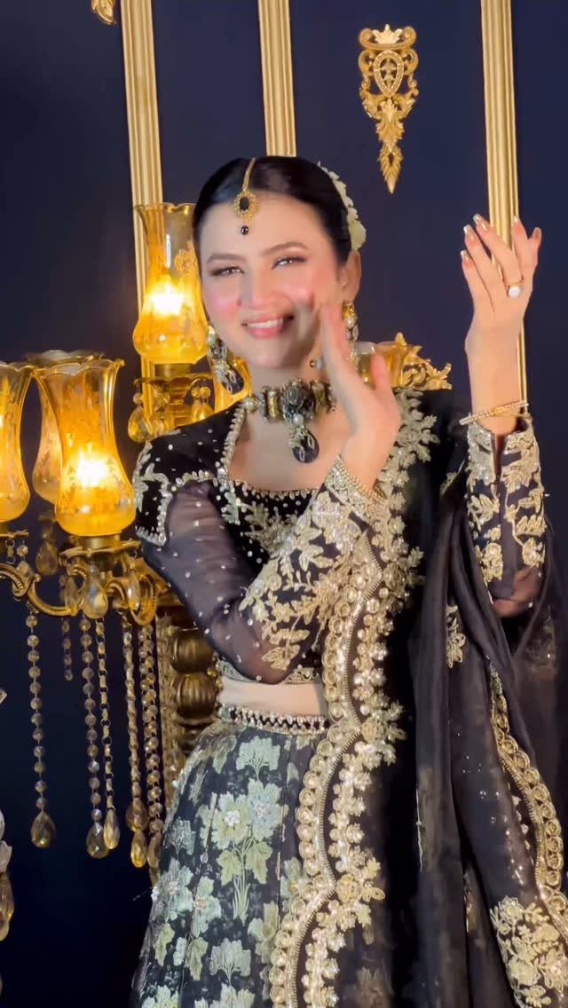 Smiling woman in a black and gold embroidered traditional lehenga set with heavy jewelry.