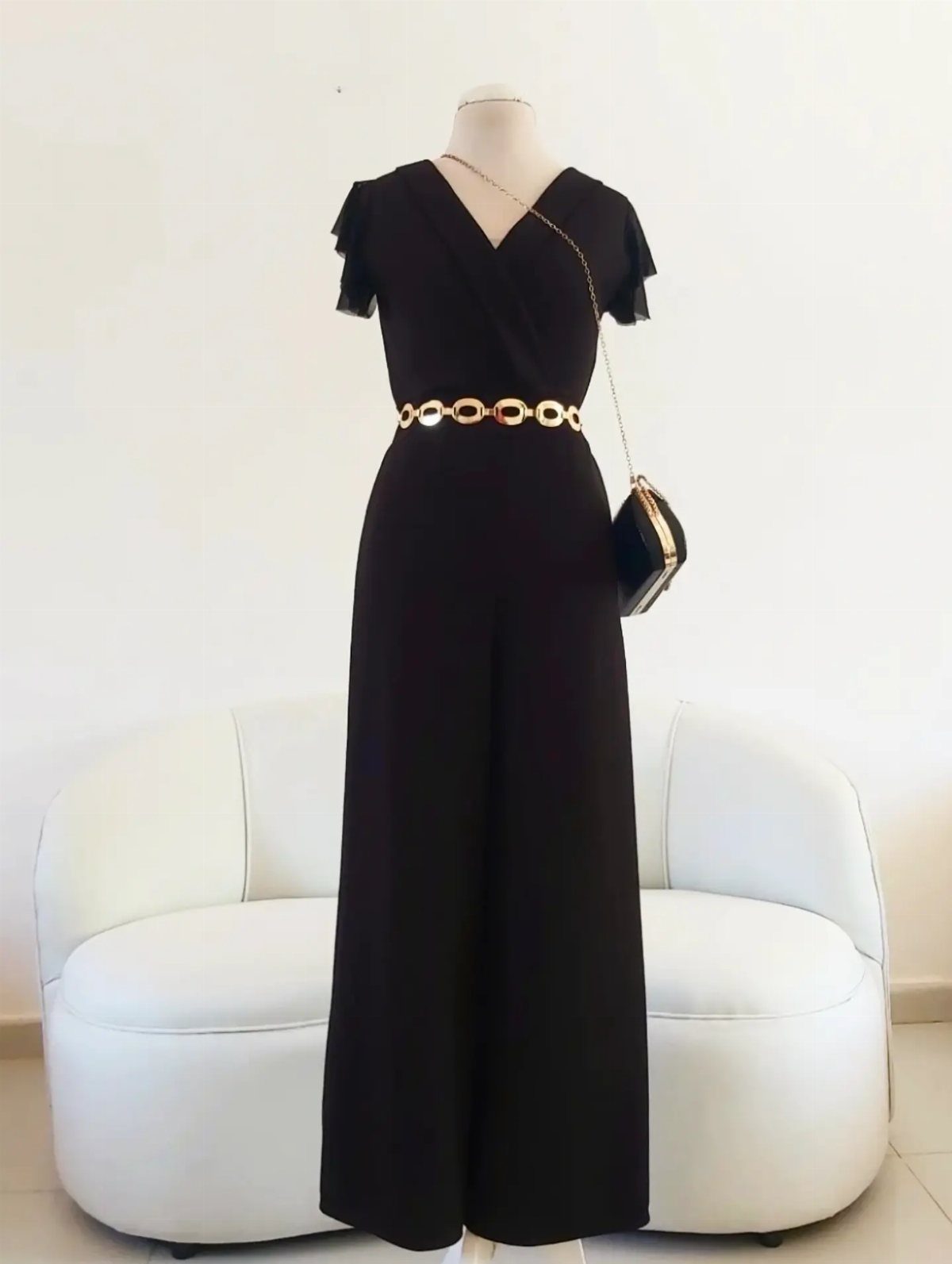 Black wide-leg jumpsuit with a gold chain belt displayed on a white mannequin.