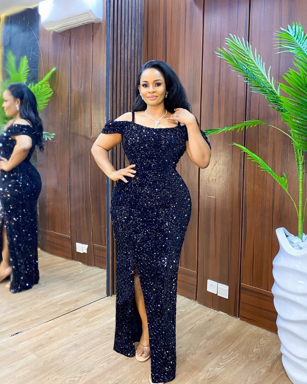 A woman wearing a long black sequined off-the-shoulder dress posing in a room.
