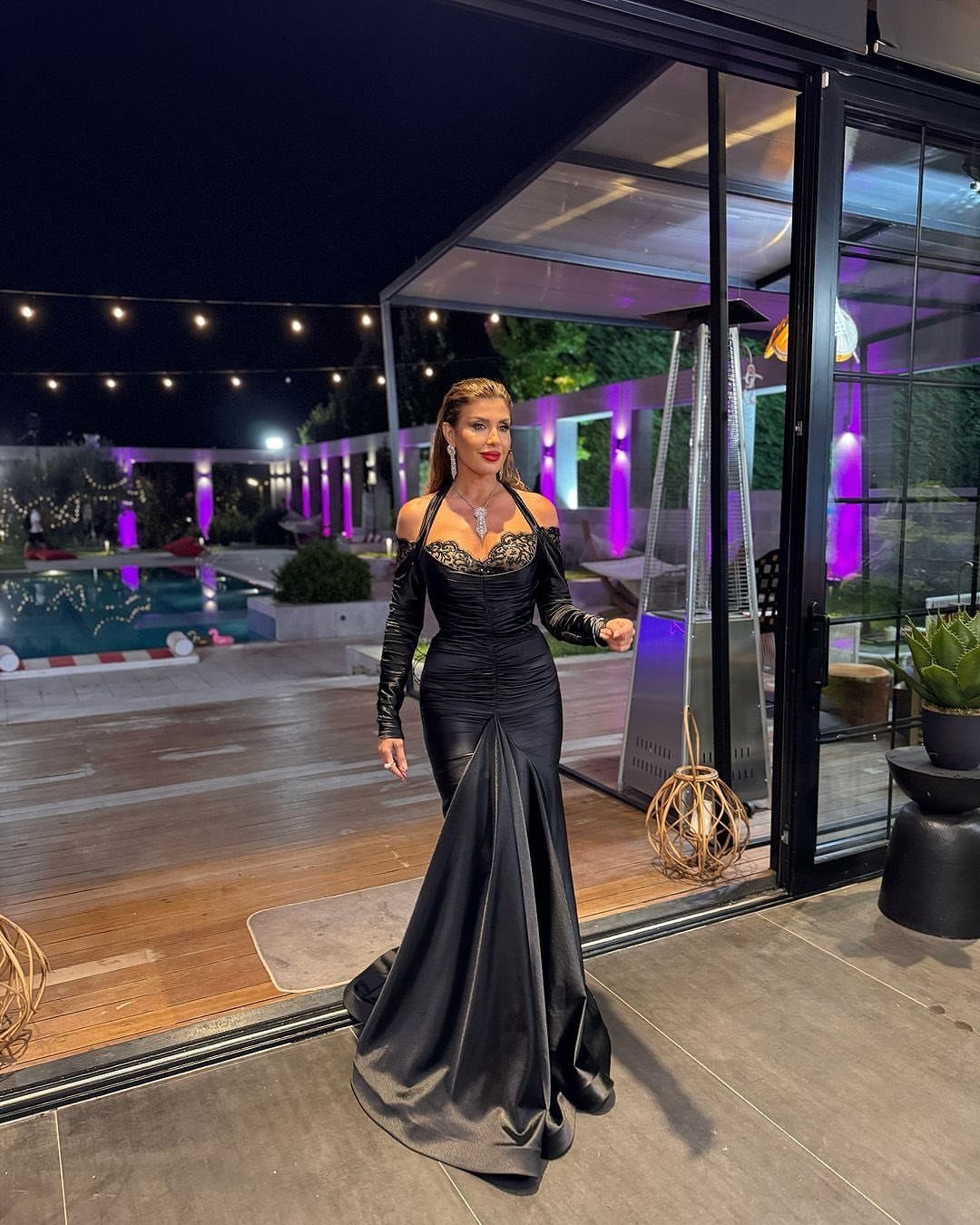 A woman wearing a long black mermaid evening gown standing on a patio at night.