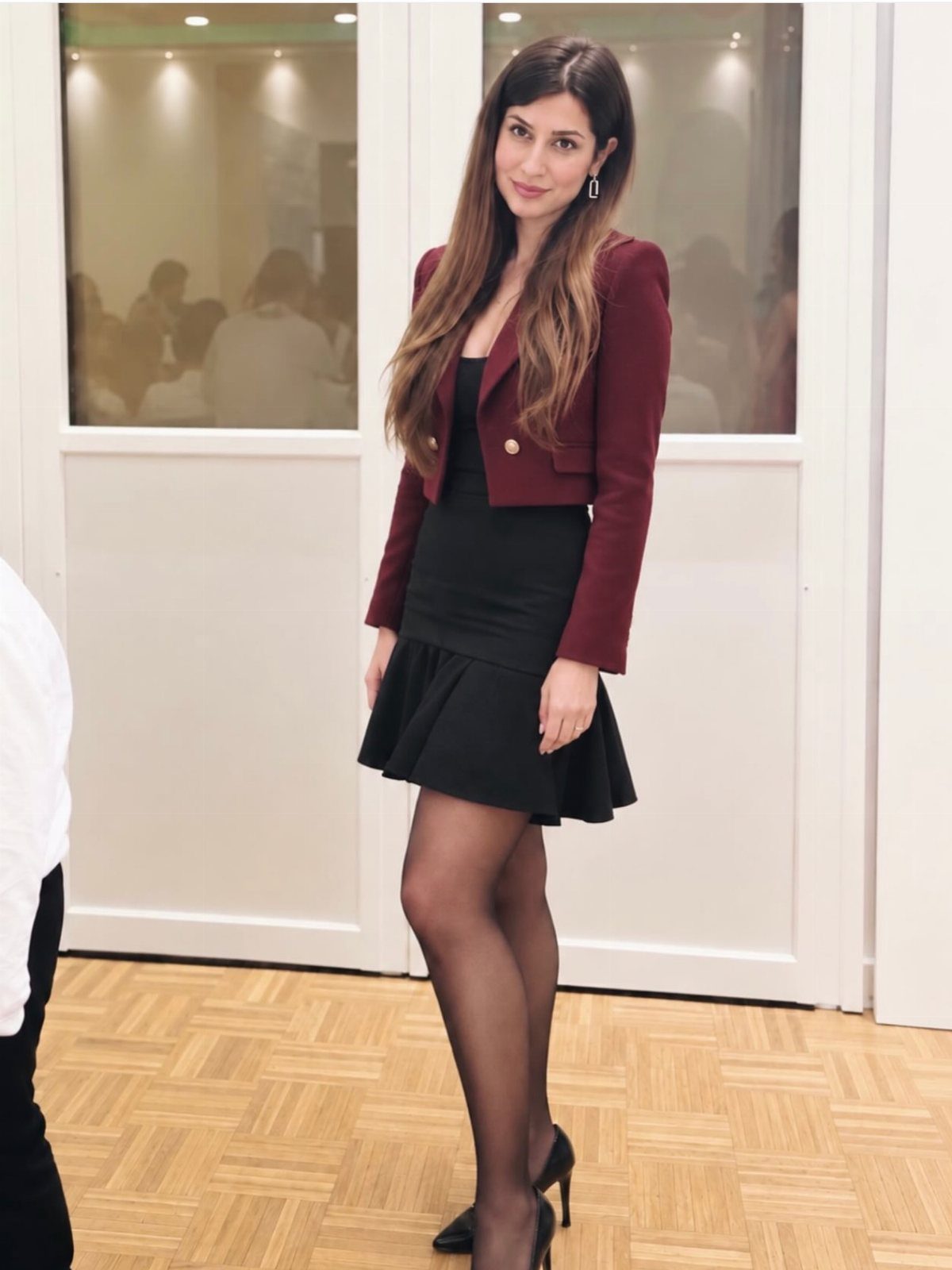 Woman wearing a maroon tailored blazer over a black ruffled mini skirt and black tights.