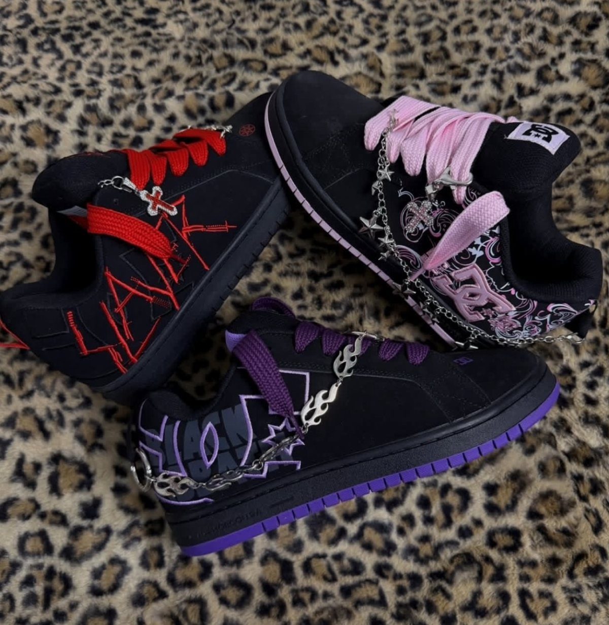 Three black sneakers with colorful laces and silver chains resting on a leopard print background.