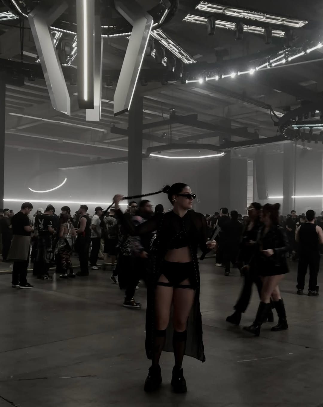 Woman wearing a black mesh rave outfit standing in a dimly lit industrial club environment.