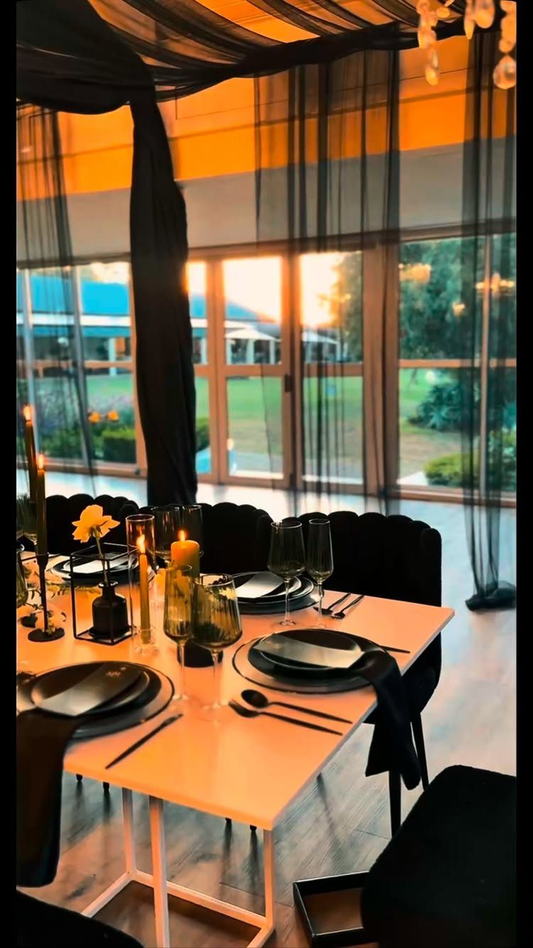 A formal dining table set with black plates and napkins against a sunset backdrop.
