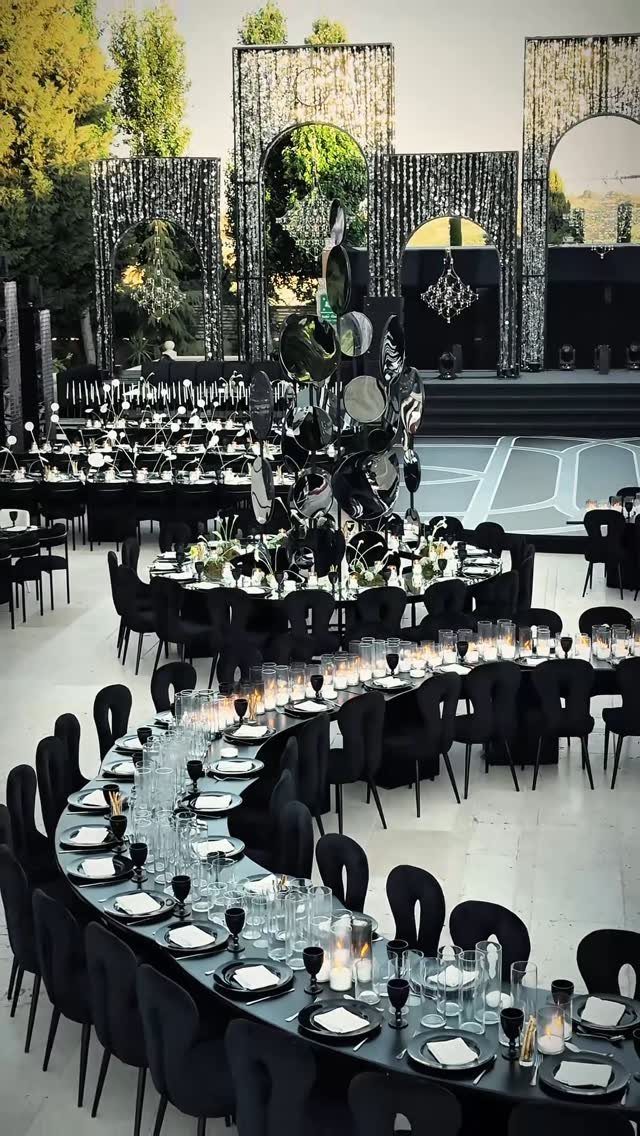 Curved black banquet tables set with white plates and glassware at an elegant outdoor evening event.