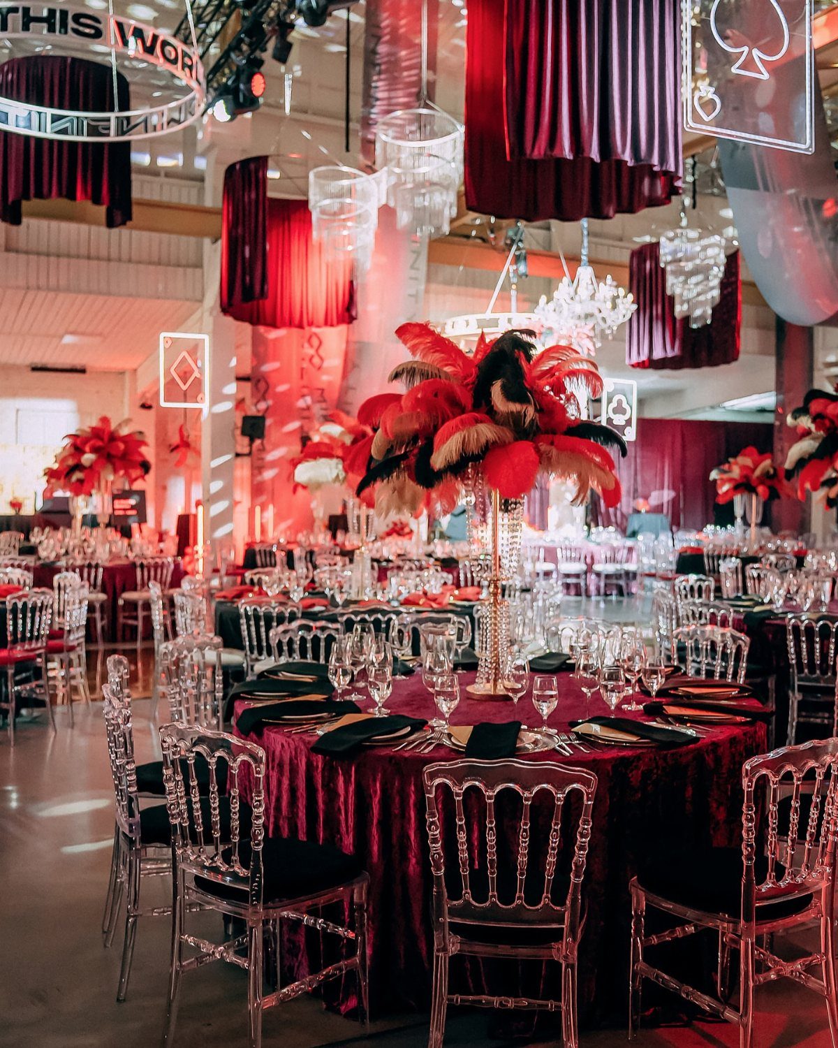 Formal banquet tables with red velvet cloths, black napkins, and large red feather centerpieces in a ballroom.
