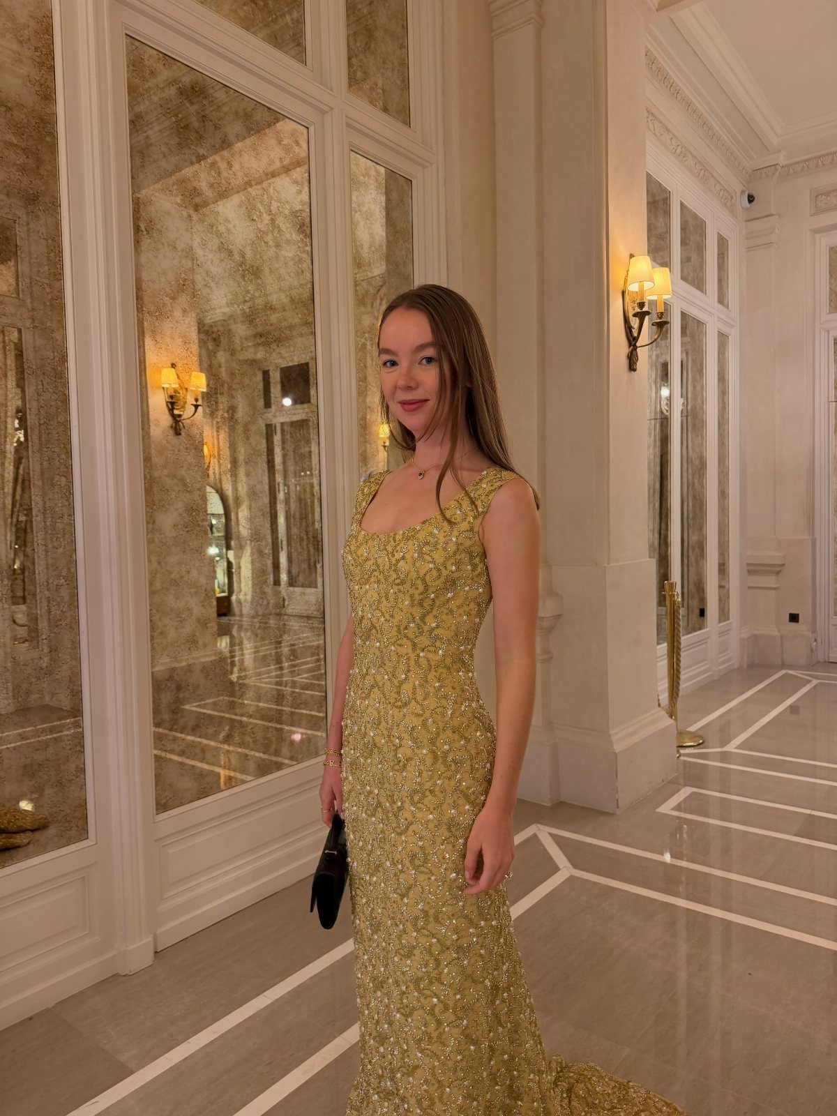 Woman in a shimmering gold sequined evening gown posing in an elegant hallway.