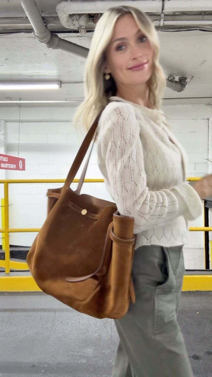 Blonde woman wearing a cream textured knit sweater and olive trousers with a large suede bag.