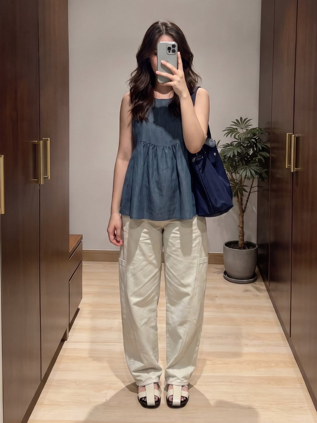 Woman in a blue peplum top and cream wide-leg trousers taking a mirror selfie.