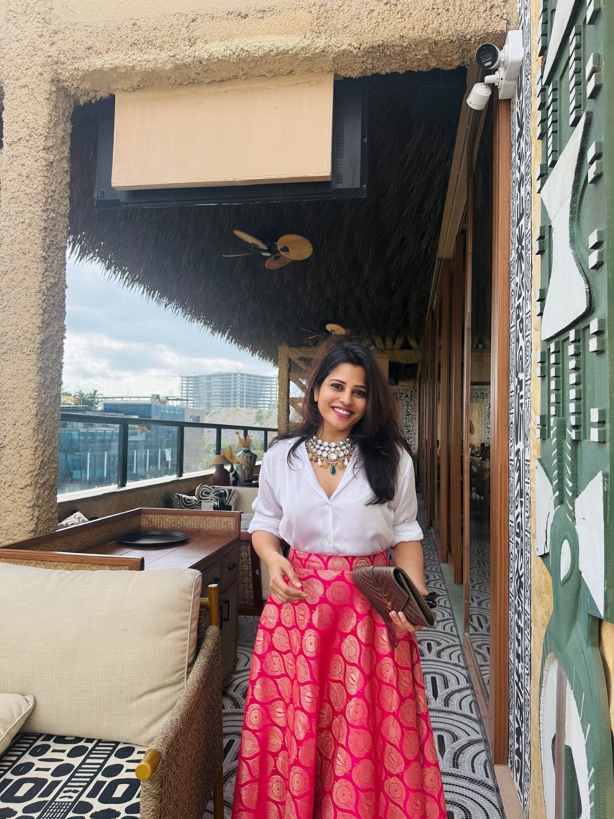 A woman wearing a white shirt and a pink patterned statement skirt standing on a balcony.