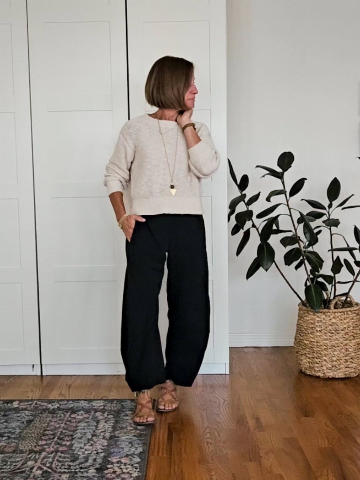 A woman wearing a cream sweater and black wide-legged pants standing in a room.