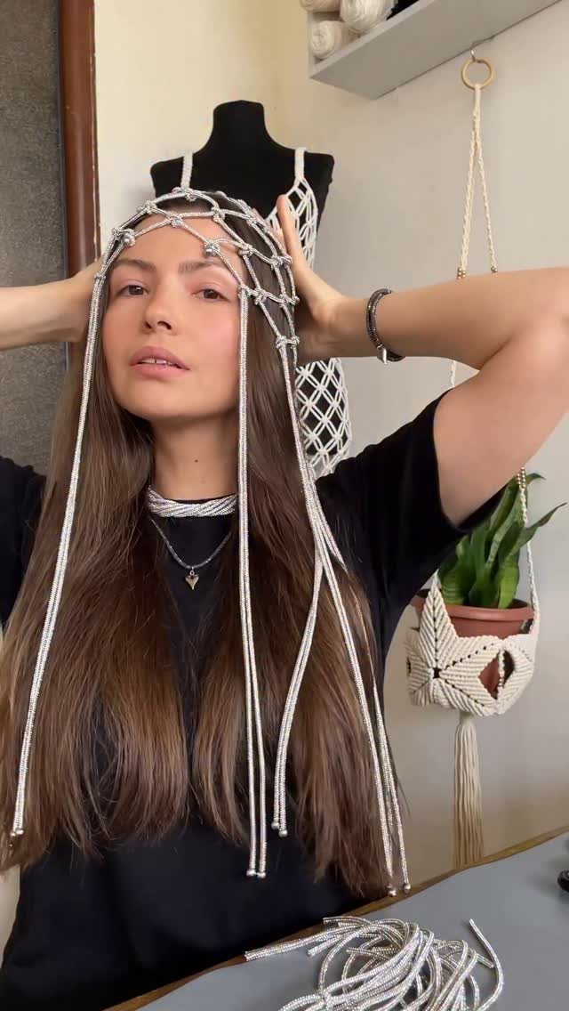 A woman wearing a white beaded headpiece with long hanging strands against a neutral background.
