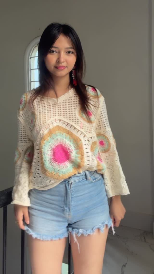 A young woman wearing a colorful crochet top and light blue denim shorts.