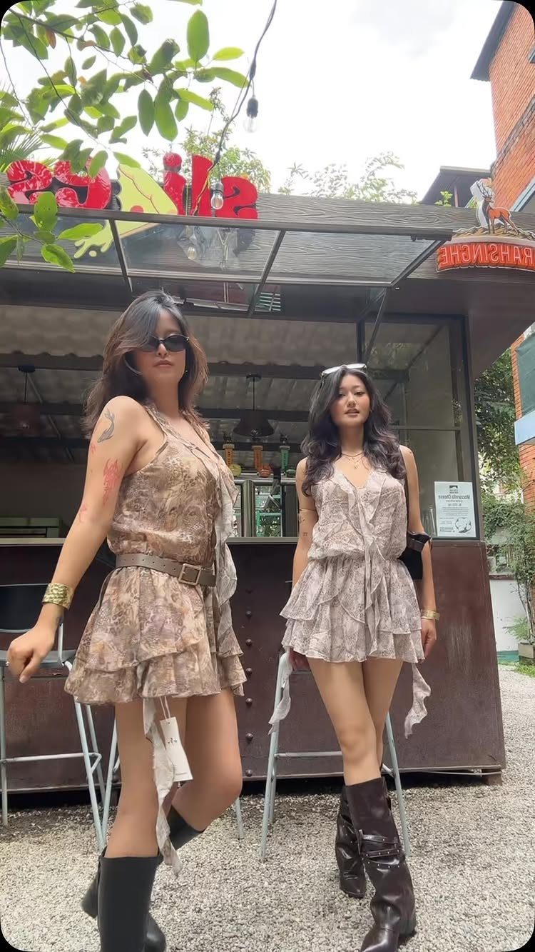 Two women posing in patterned, ruffled romantic mini dresses and dark boots outdoors.