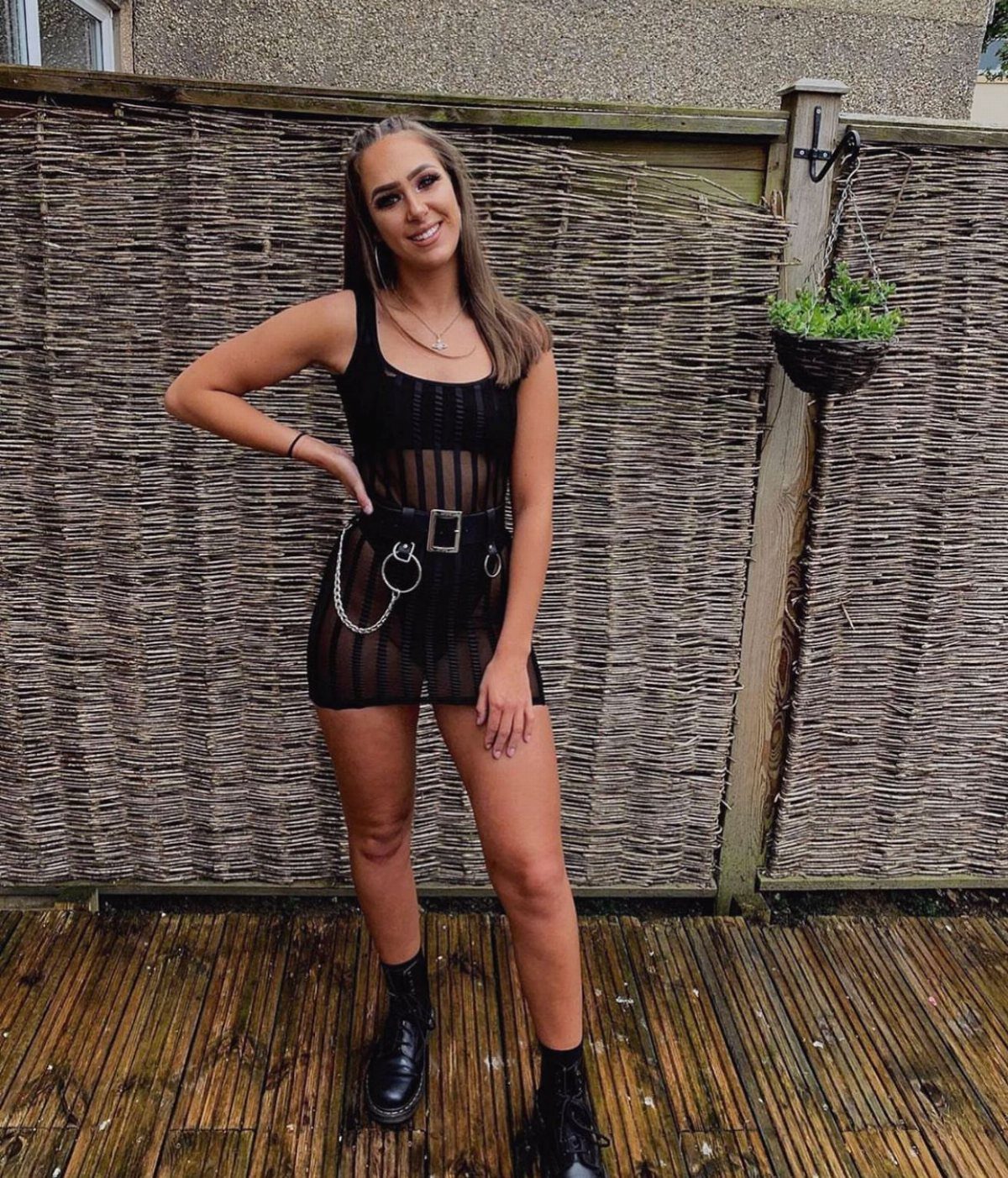 A smiling woman wearing a black sheer mini dress and black combat boots outdoors.