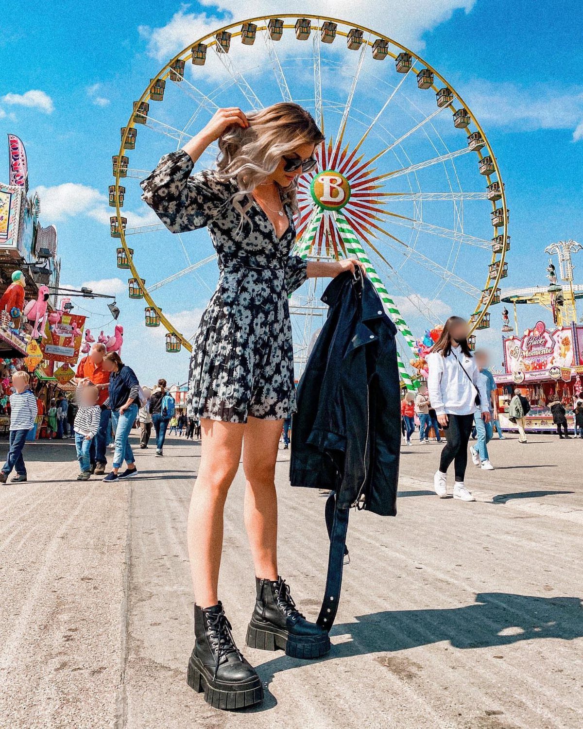 Woman in a black and white floral printed dress posing in front of a Ferris wheel.