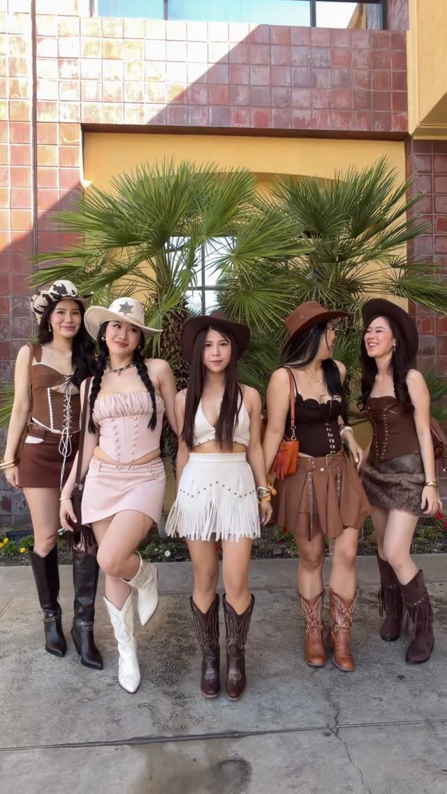 Five women posing in boho festival outfits and cowboy boots in front of palm trees.