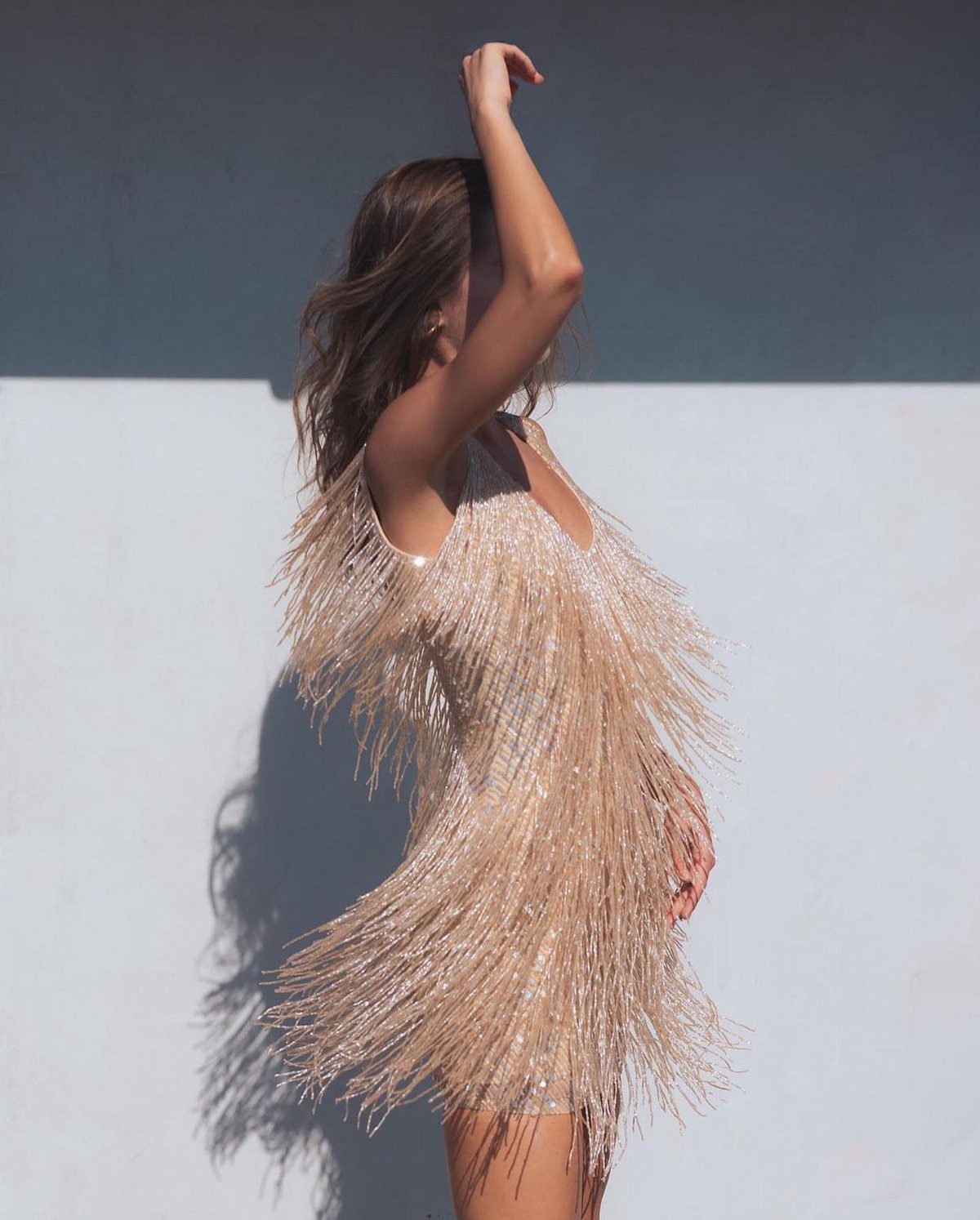 Woman in a shimmering champagne fringe cocktail dress posing against a two-tone wall.