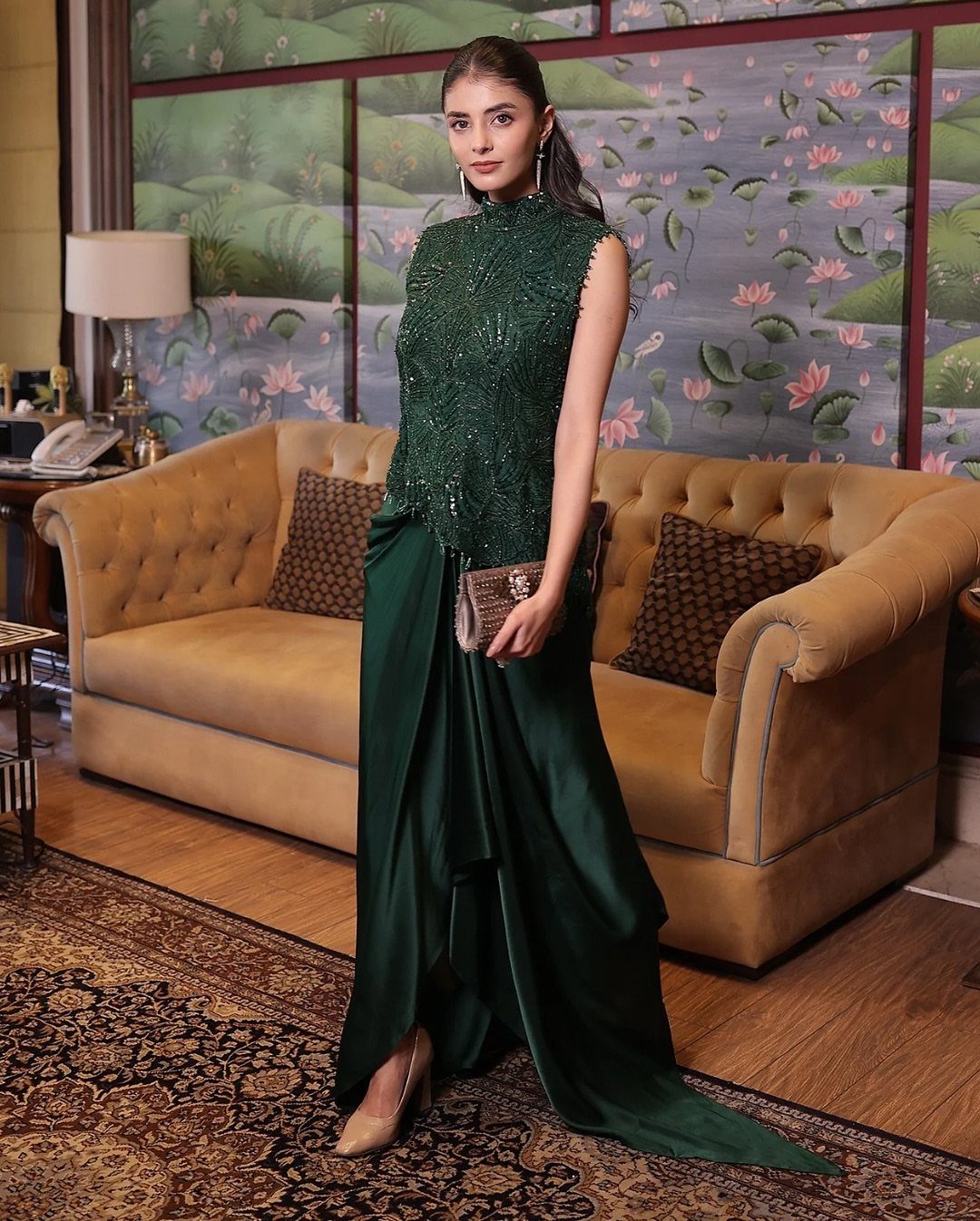 Woman in an emerald green sequined top and satin skirt posing in a living room.