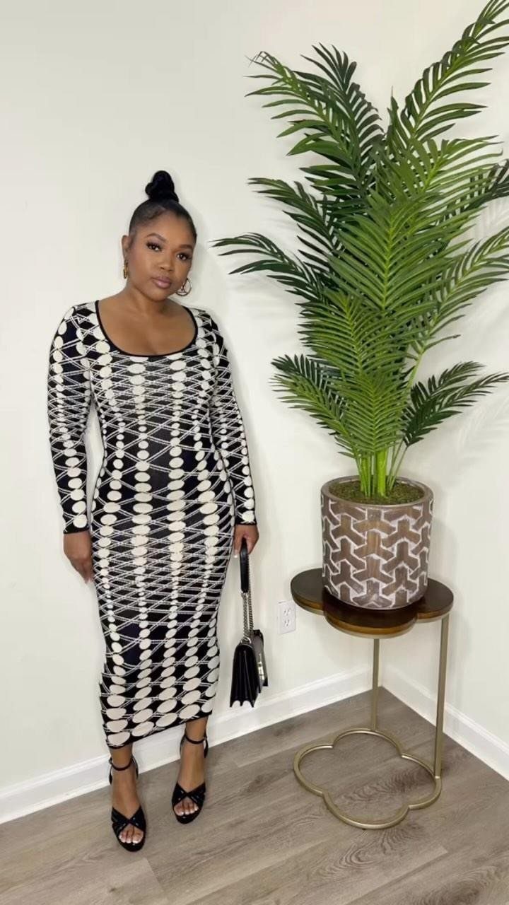 A woman posing in a black and white patterned long-sleeved sweater dress.