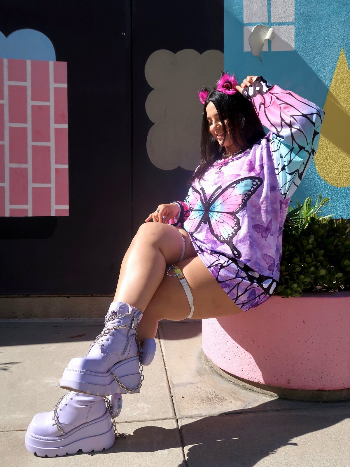 Woman in purple butterfly print top and lavender platform boots sitting against a colorful wall.
