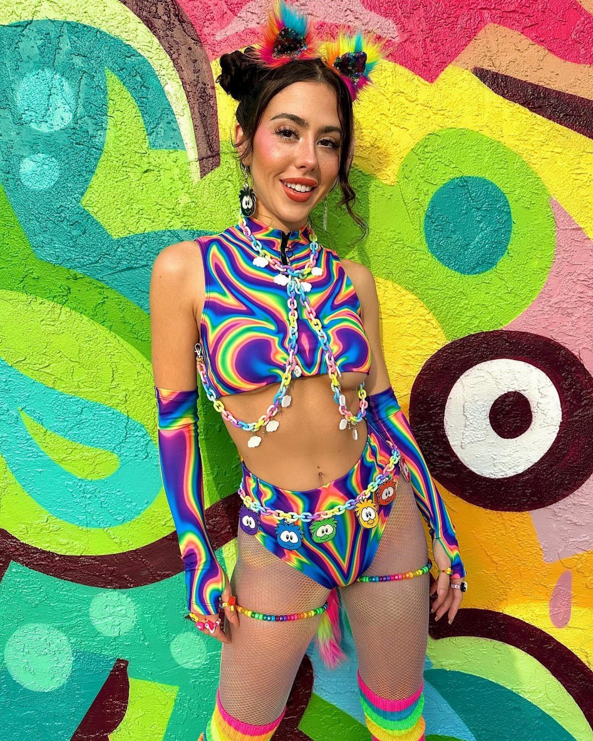 Woman in a psychedelic rainbow swirl crop top and matching bottoms posing against graffiti.