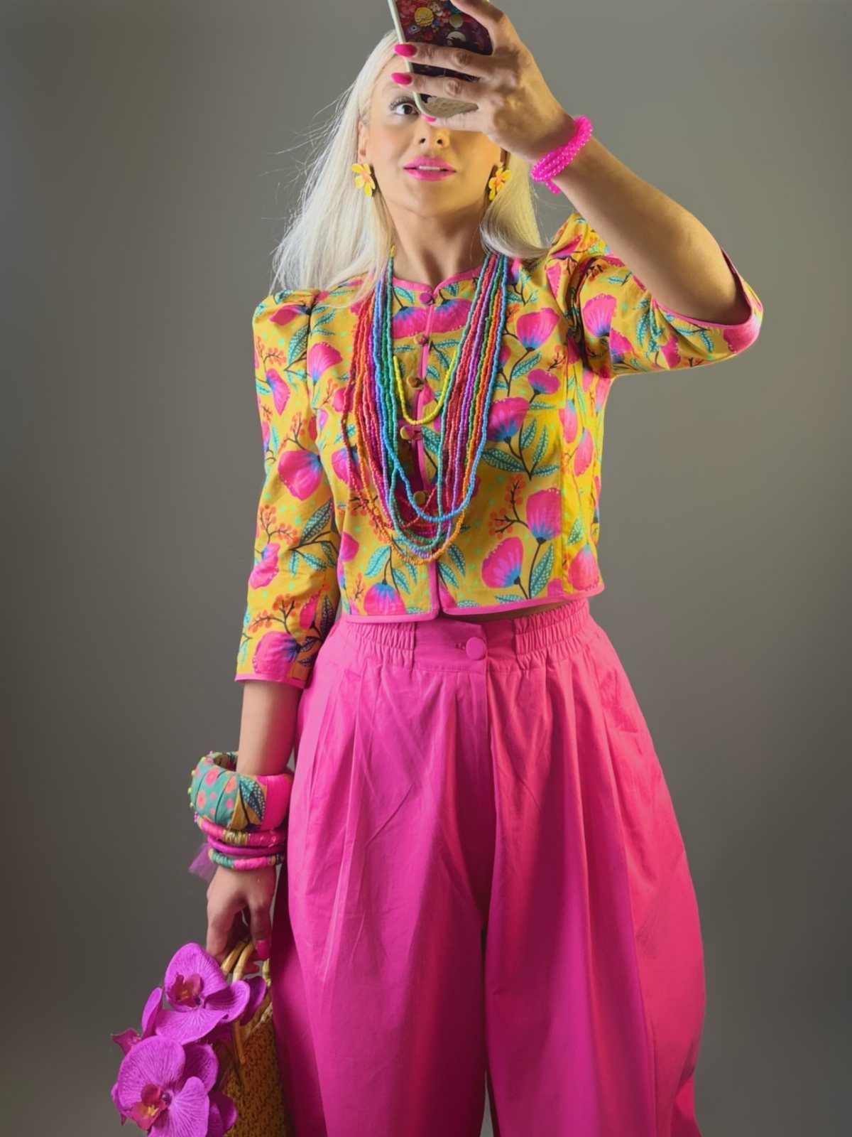 Woman in a colorful floral jacket and bright pink high-waisted trousers posing for a selfie.