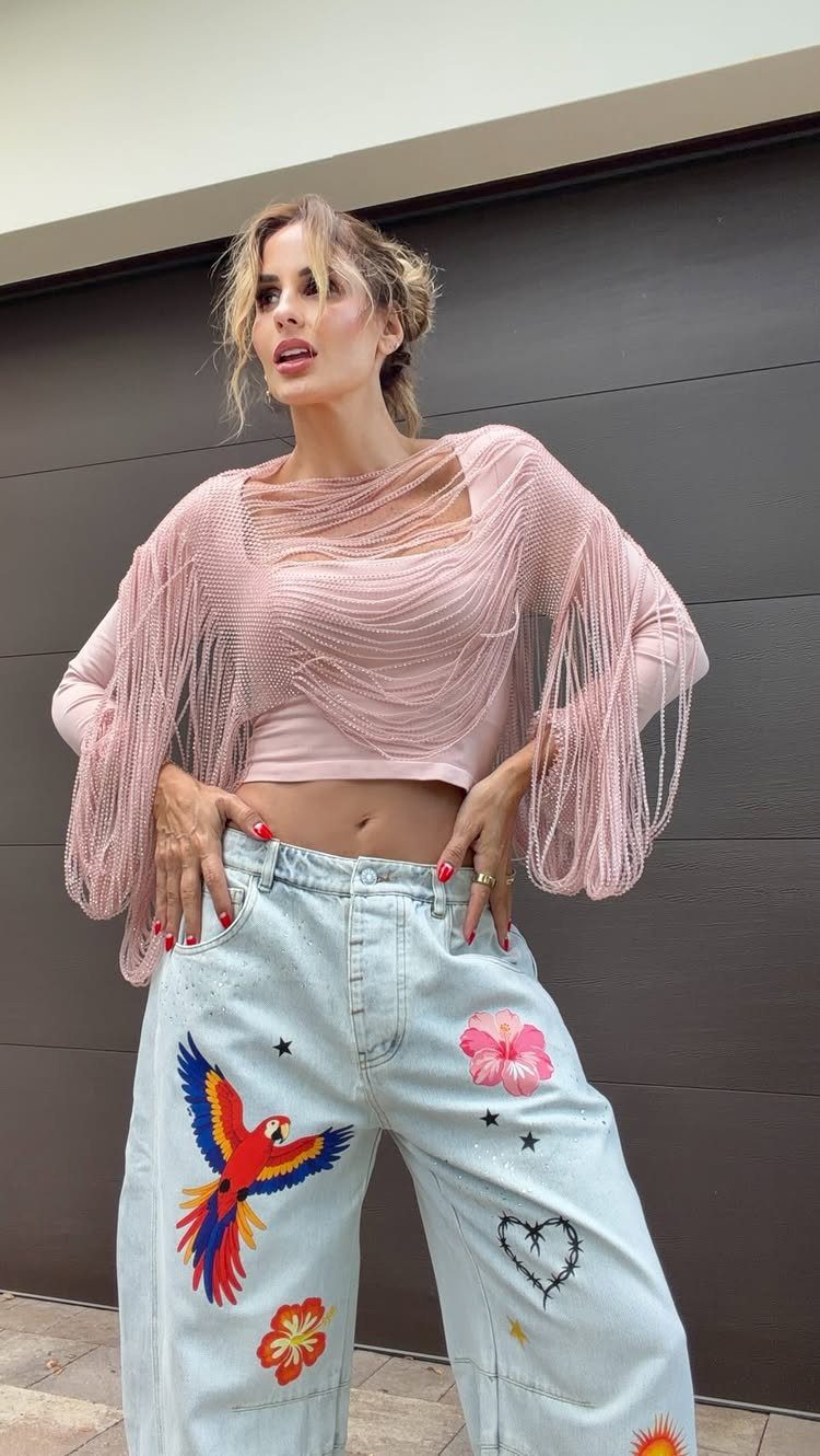 Woman wearing a pink fringed crop top and embroidered light blue high-waisted denim jeans.