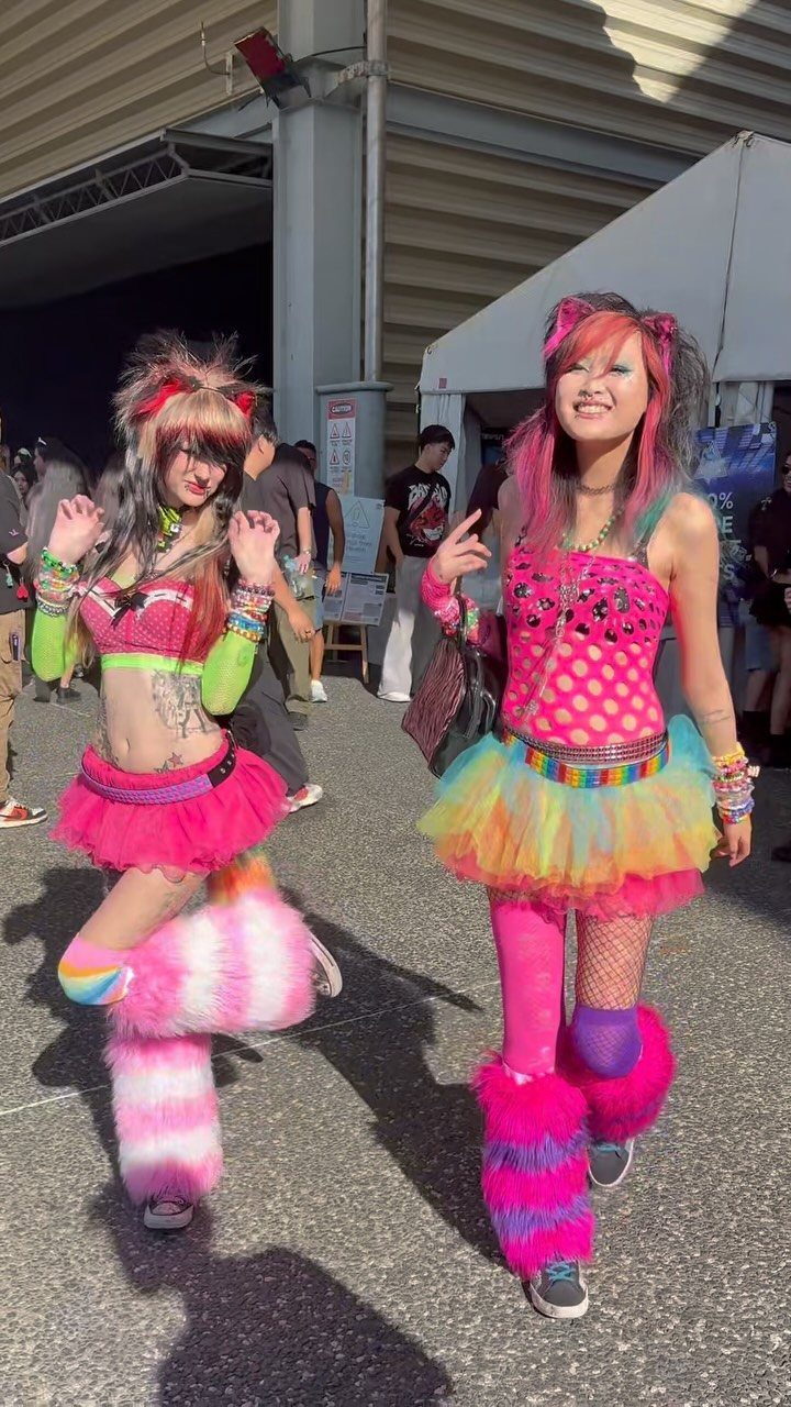Two women posing in bright, colorful rainbow and pink concert outfits with fuzzy leg warmers.