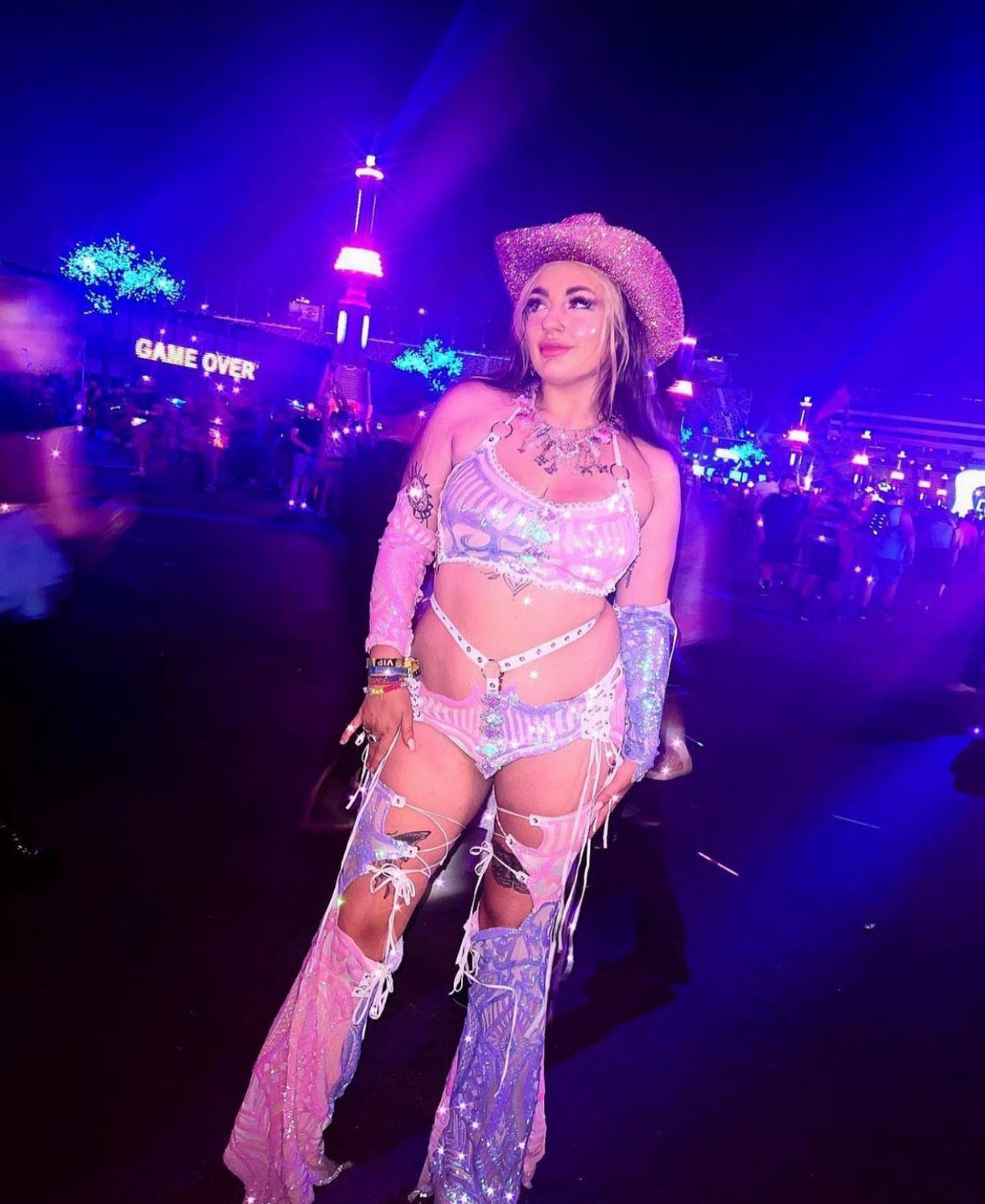 Woman in a sparkly pink and blue festival outfit posing under blue lights.