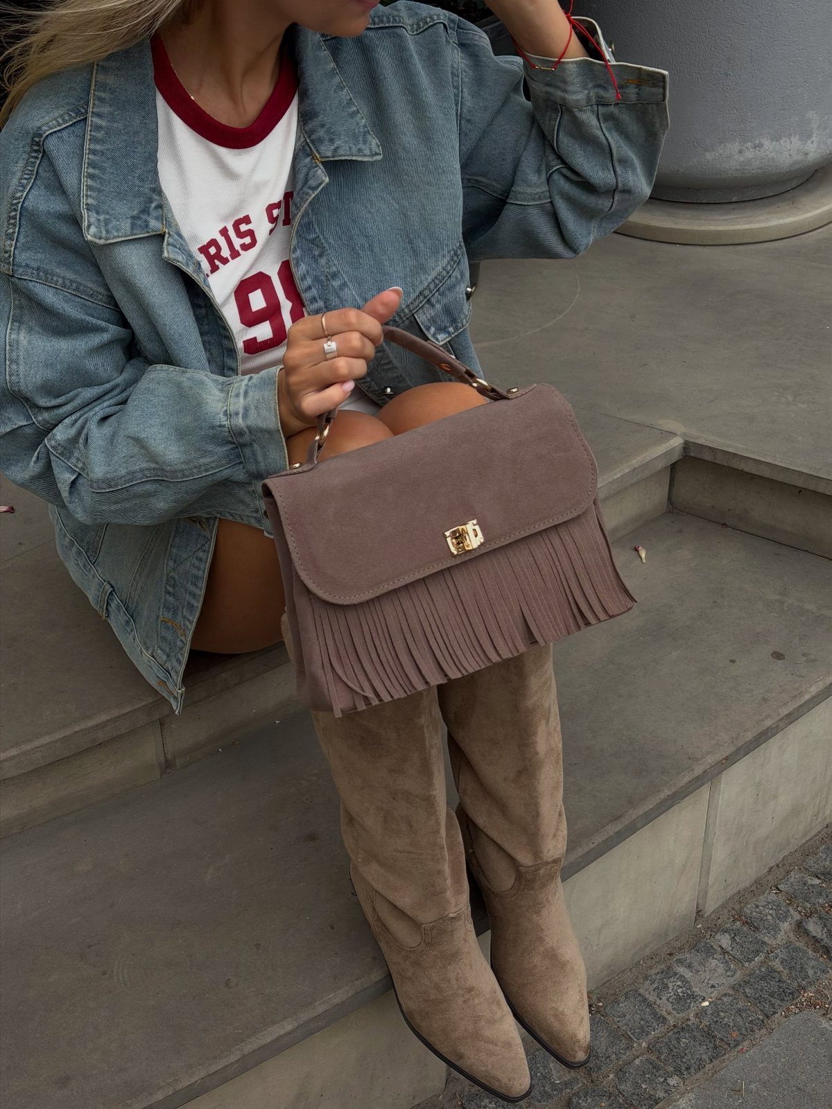 Person sitting on steps wearing a denim jacket, shorts, and tall tan suede boots.