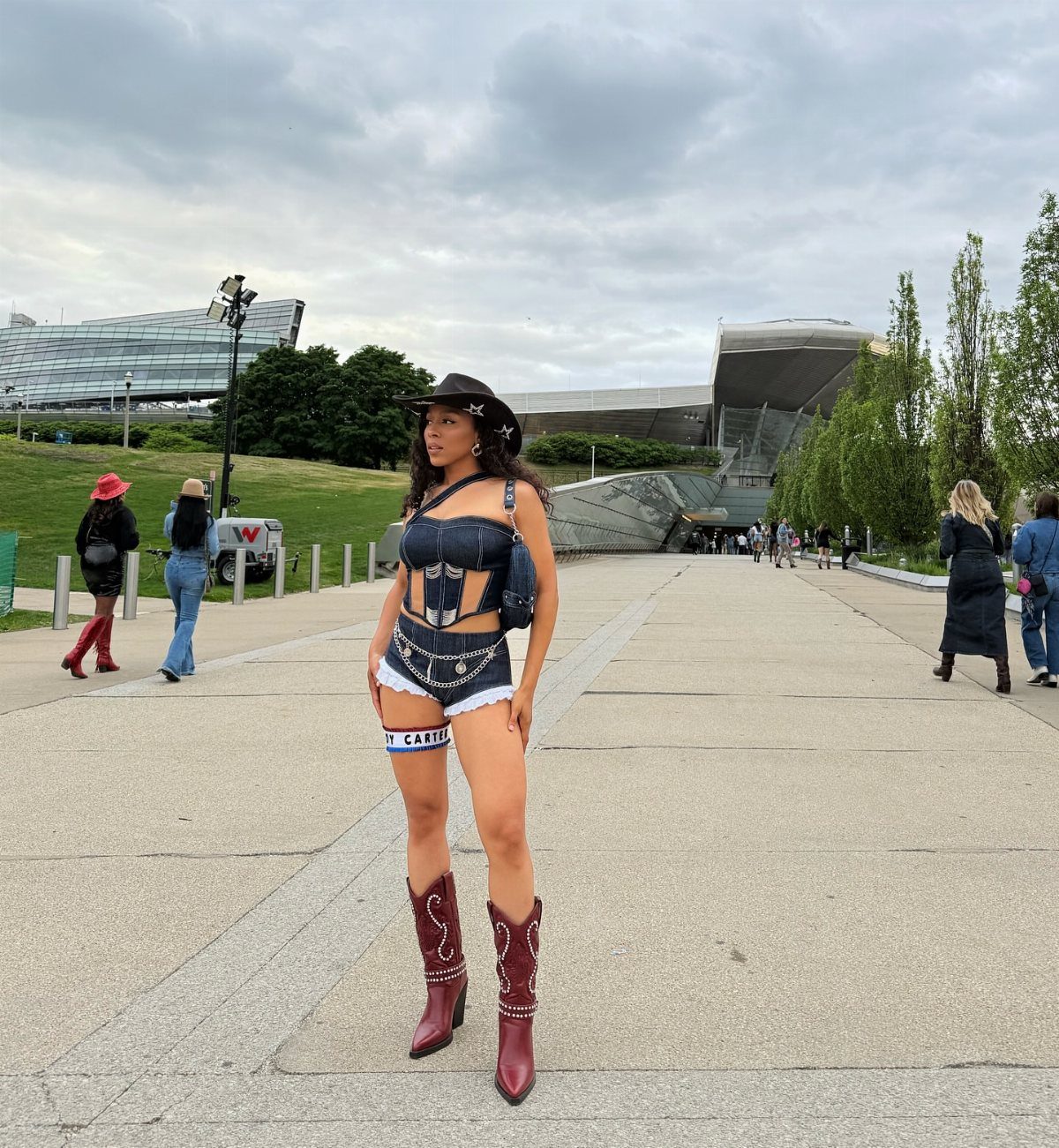 Woman in denim outfit and red cowboy boots posing on a paved walkway outdoors.