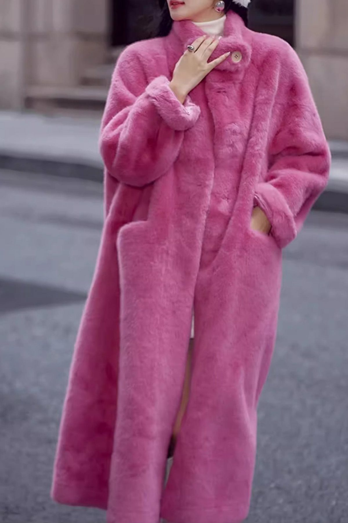 A person wearing a long, voluminous pink faux fur coat standing on a street.