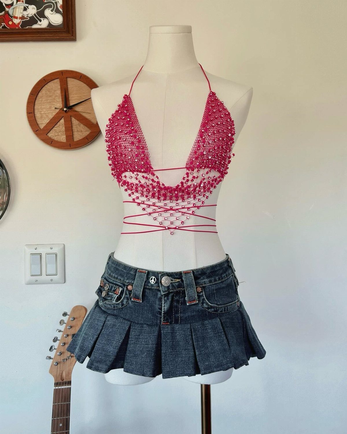 A mannequin wearing a pink sequined halter top and a denim pleated mini skirt.